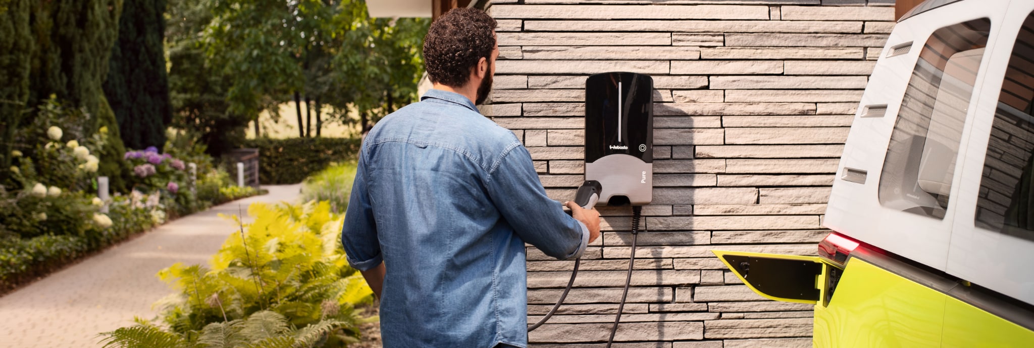 Elektromobilität Zuhause: Ein Mann im Jeanshemd wie er an einer Wallbox im Garten ist