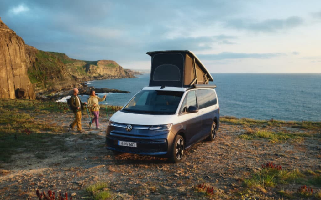 Camper-Vermietung 1 Camper-Vermietung - Blau-weißer VW T7 California Ocean mit Falt-Dach an steiler Klippe mit Meerblick