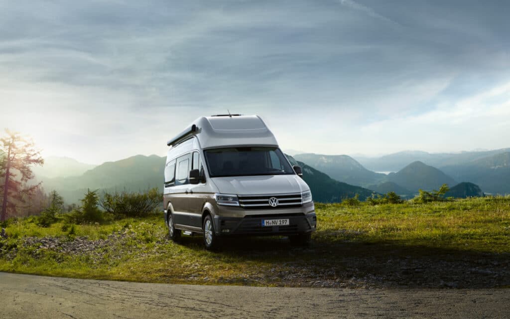 Camper-Vermietung 2 Camper-Vermietung Weiß-brauner VW Grand California Campervan auf grüner Wiese in den Bergen